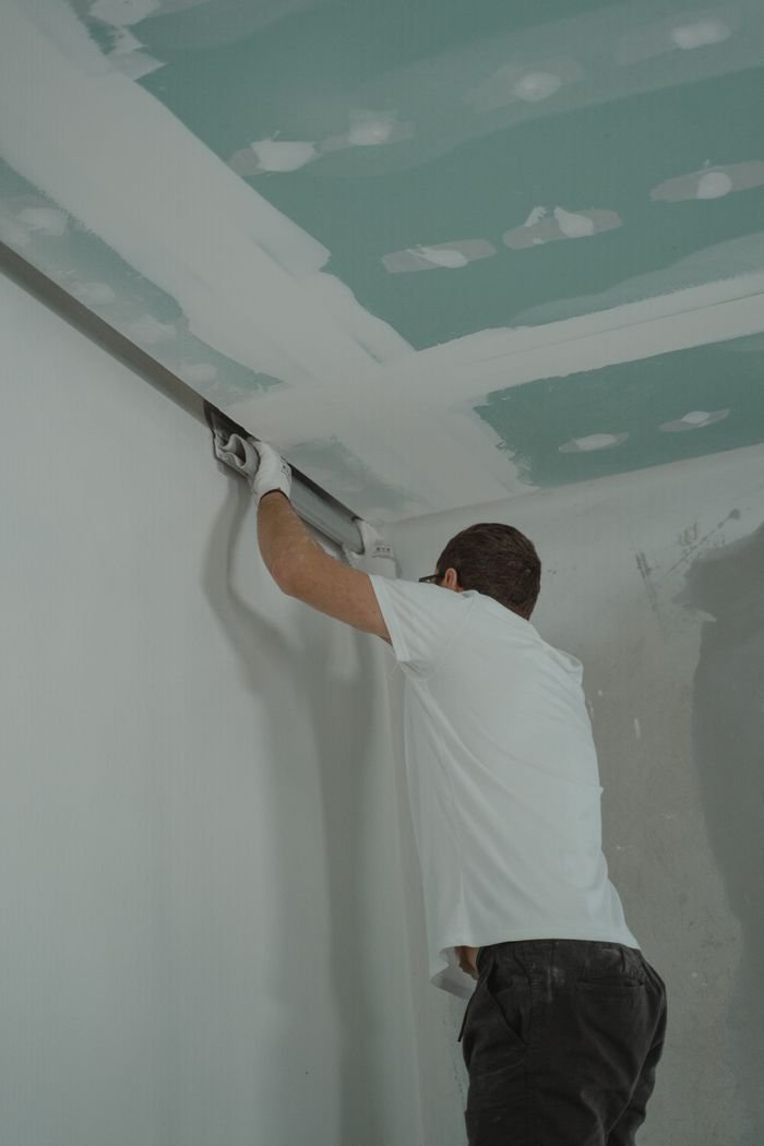 Home A man works meticulously on drywall installation during a house renovation.