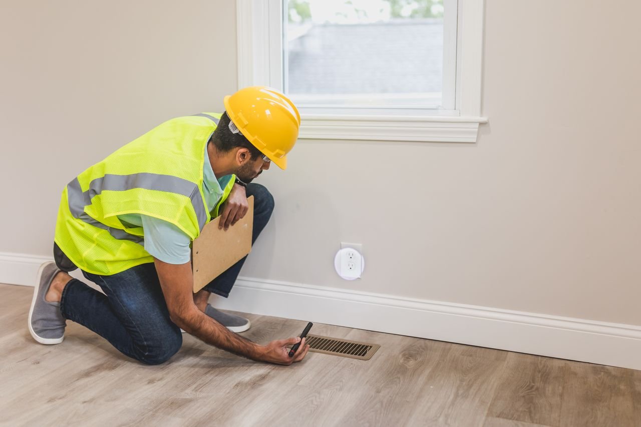 Crafting Captivating Headlines: Your awesome post title goes here A construction worker in a hard hat inspects a floor vent indoors, ensuring quality and safety standards.