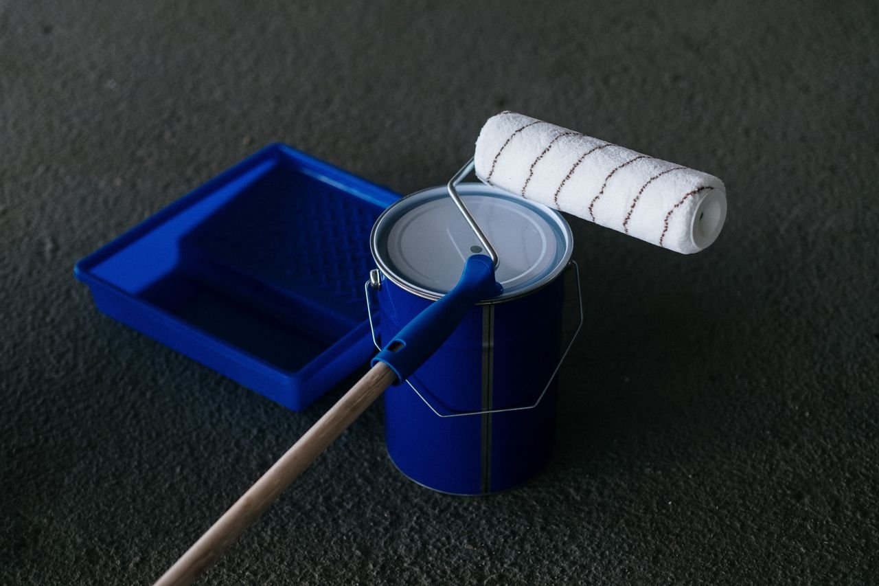 Home Close-up of a paint can, roller, and tray on a textured floor, perfect for DIY projects.